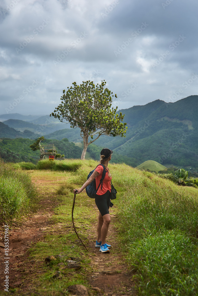Naklejka premium Beautiful European woman hiking in La Vallée de Ferney, Mauritius. Outdoor adventure in lush tropical forest with scenic mountain views. Active lifestyle and nature exploration.