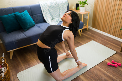Young woman performing ustrasana or camel yoga pose at home