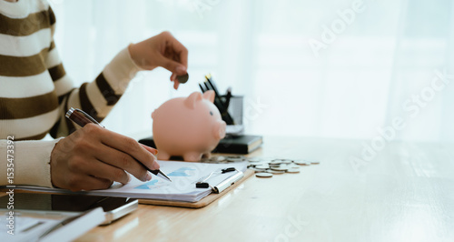 An Asian woman is putting money in a piggy bank while looking at a calculator, giving advice on financial planning.