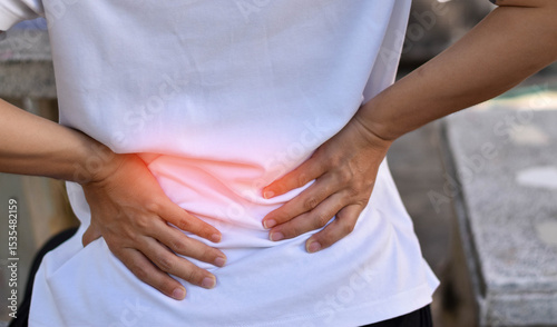 Back pain concept. Person holding their lower back with both hands, indicating discomfort or injury related to back muscles, spine, or kidney issues.