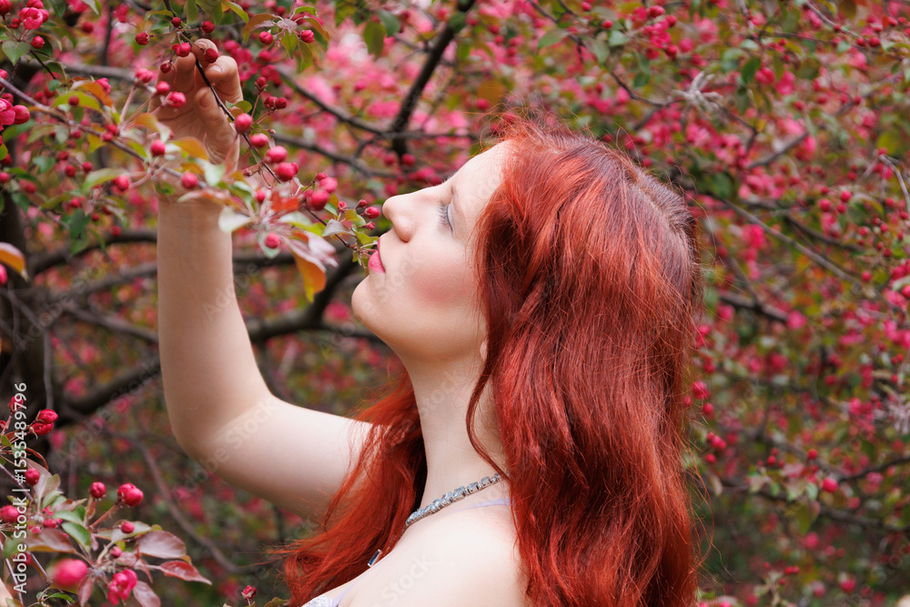 Naklejka premium red-haired girl with curly hair walks in the park. Girl in a smart dress smiles. Woman poses against the background of blooming pink apple trees in a turquoise dress