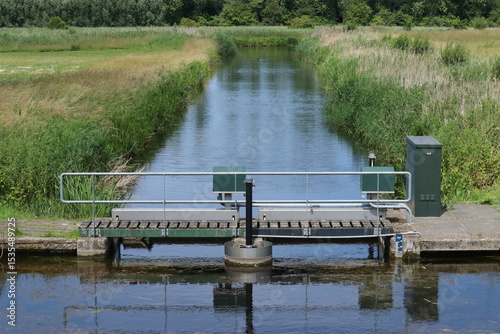 a canal with water and a weir with a gangway in a nature reserve in the dutch countryside