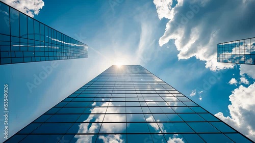 Glass skyscraper reflecting clouds and sun with upward view toward blue sky on bright day in modern cityscape