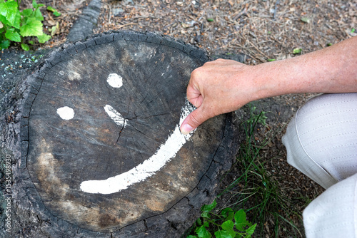 A woman draws a caricature of a face on a tree stump with the tip of her finger.