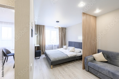 modern, light-filled studio apartment with a gray bed, couch, and wooden slat partition. A separate area is visible in the background