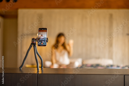 A smartphone on a tripod captures a woman in pajamas creating video content. Great for illustrating influencer work, home blogging, or remote lifestyle content creation