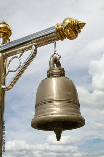 brass bell hanging from a pole on a sky background.