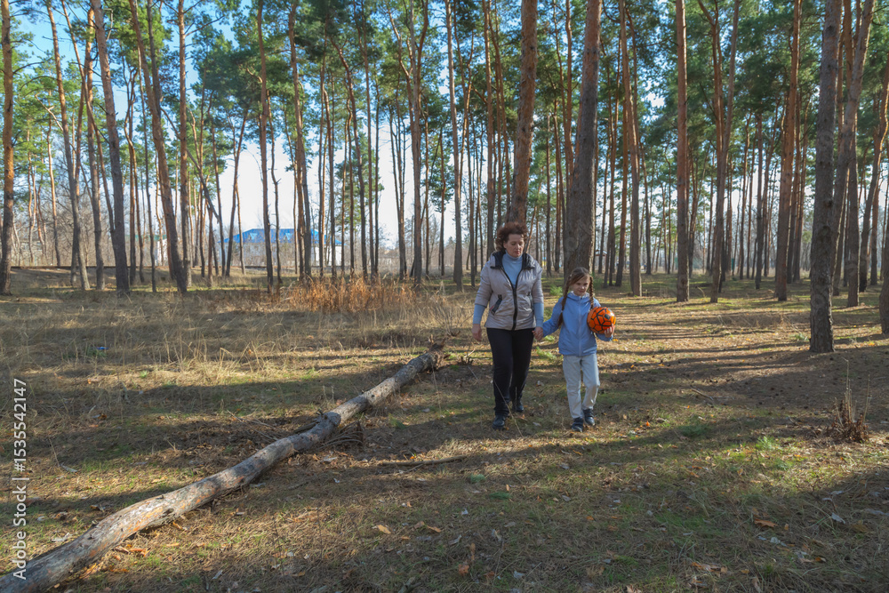Obraz premium Grandmother and granddaughter walking in forest holding sports ball on sunny day