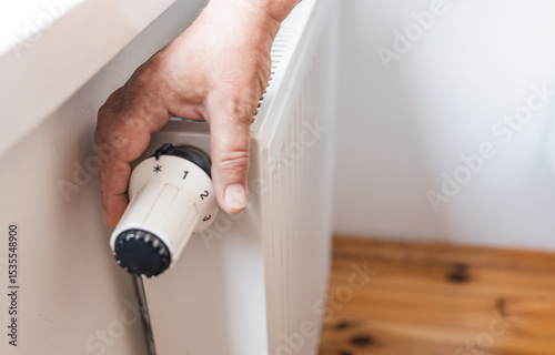 Hand regulates the heat  in the house on the radiator handle.