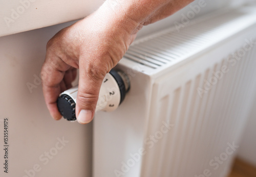 Hand regulates the heat  in the house on the radiator handle.
