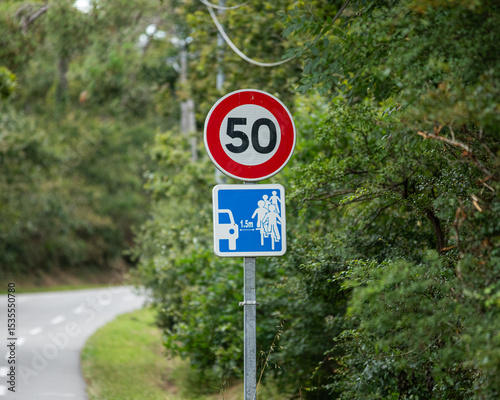 Un panneau de limitation de vitesse indiquant 50 km/h se trouve le long d'une route. Un autre panneau signale la proximité d'un chemin pour cyclistes, avec une distance de 1,5 mètre.