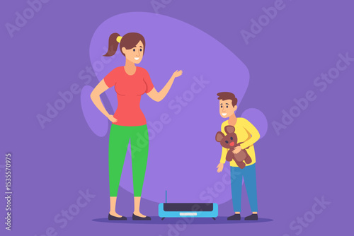 Young boy holding teddy bear and interacting with robotic device on floor as his mother standing nearby, engaging in conversation, in brightly colored room