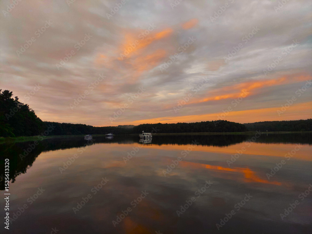 Obraz premium dramatic sunset over a tranquil lake with a few boats