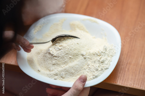 Mixing semolina flour with sugar using a metal spoon in a white ceramic bowl for cake preparation on a kitchen table