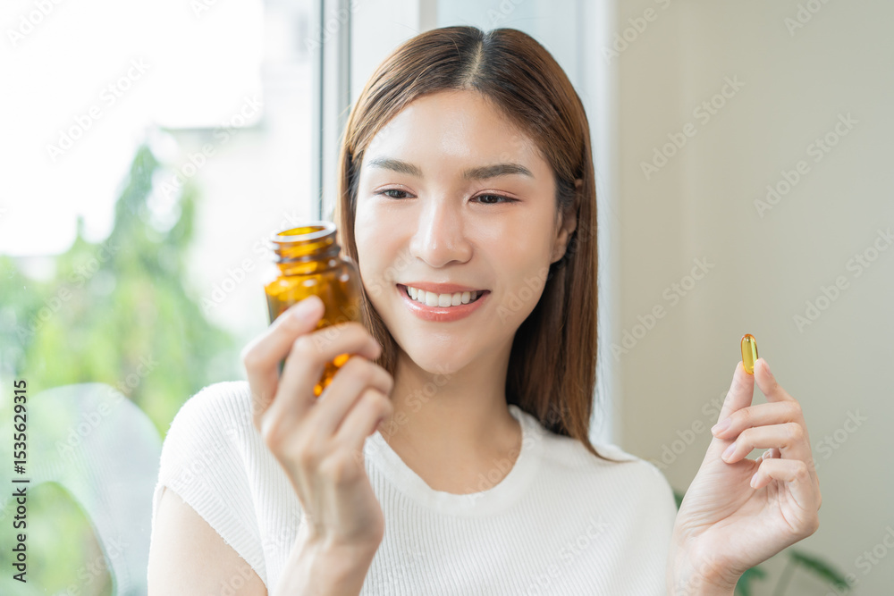 Fototapeta premium Dietary supplement concept, happy asian young woman hand holding fish oil pills, drugs medical tablet pouring capsules from medication bottle, take vitamin treatment for skin, hair at home, healthcare