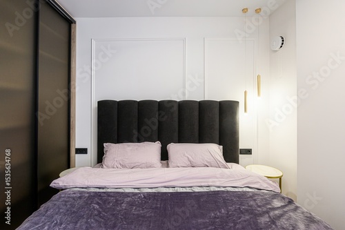 Wallpaper Mural modern bedroom featuring a dark upholstered headboard, soft bedding, gray curtains, and a unique circular light fixture. The room has white walls with paneling and a light wood floor Torontodigital.ca