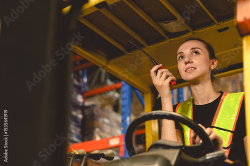 warehouse, radio, and forklift in shipping warehouse. Female transport worker in safety uniform transport worker talking on walkie talkie, drives forklift at freight cargo warehouse port.