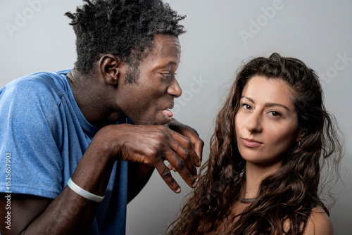 Annoyed woman looking at camera while her partner bothers her with a funny, goofy face.