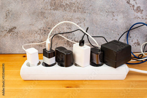 Many smartphone or tablet chargers plugged in a big extension cord outlet on  wooden floor with gray stucco, soft focus close up