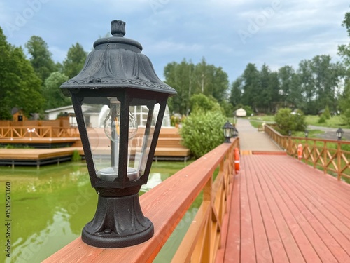Fototapeta Naklejka Na Ścianę i Meble -  A black street lamp stands on a wooden bridge on a warm sunny day. High quality photo