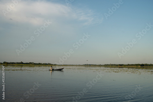 Konstfotografi A lone boater on vast calm water with a clear sky and distant horizon conveying