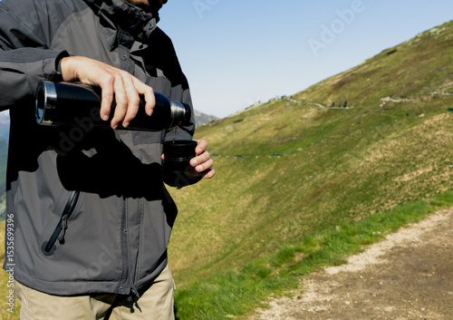 man pouring tea from thermos against mountain range background, hiking in mountains 