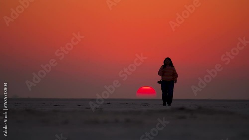Silhouette shot of Teenager girl walking on desert land at Kutch, Gujarat, India. Girl go against the background of the orange sun with copy space. Woman in the desert with sunset view.
