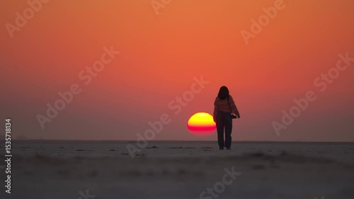 Silhouette of Indian girl raise hands and celebrate success. Sunset shot of girl standing at white desert of Kutch in Gujarat, India. Powerful, confident and successful woman concept.