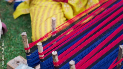 Indian woman weaving traditional handicraft clothes in a village. Woman weaving colorful shawl in open garden. Indian culture concept.