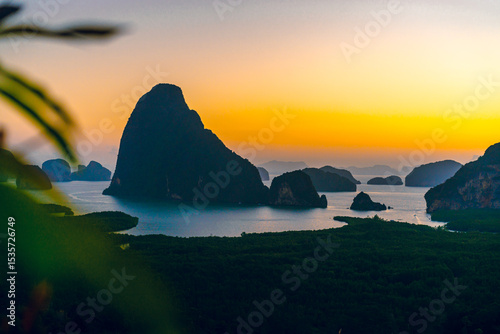 Numerous limestone mountains in the bay in Phang Nga Province, Thailand. The light of the sky is colorful of rising sun in the early morning. There is a blurred foreground of grass on the left. photo