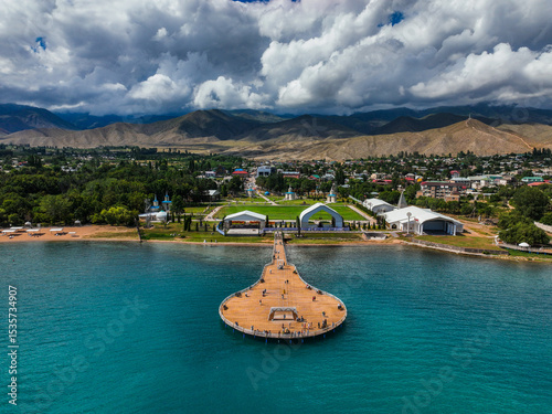 Expansive aerial view of the Komuz shaped pier leading to the Rukh Ordo Cultural Center on the shores of Issyk Kul Lake, with mountains in the background
