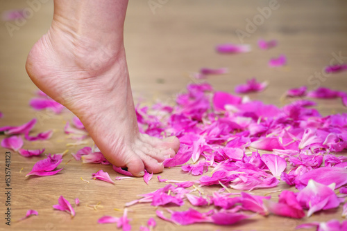 A woman's foot gently steps on scattered pink rose petals, embodying tenderness, femininity, and self-care