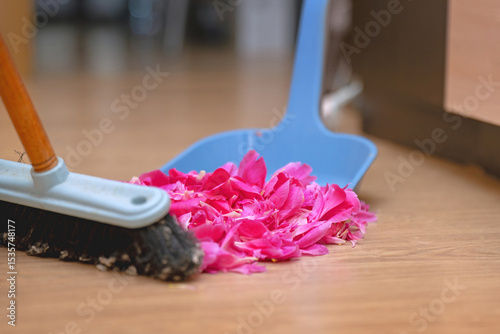 Sweeping pink rose petals with a brush into a dustpan, symbolizing the end of a romantic relationship