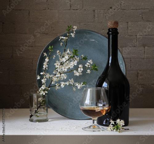 Still life with a bottle of wine and a blooming cherry twig.