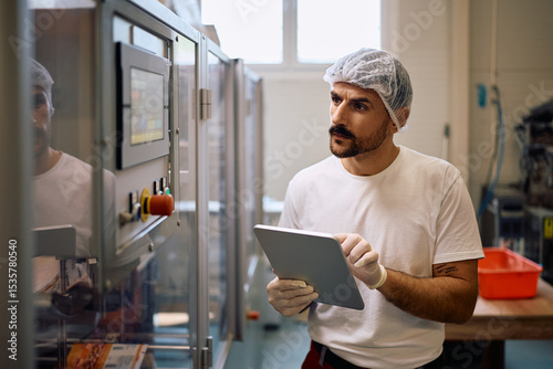 Worker using digital tablet while supervising the processing machine in a factory.