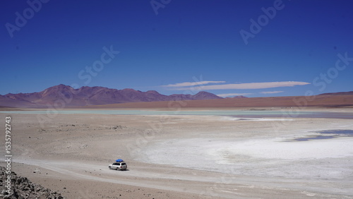 Colorful Bolivian lagoon surrounded by dramatic mountains, salt flats, flamingos, and off-road explorers in the remote altiplano