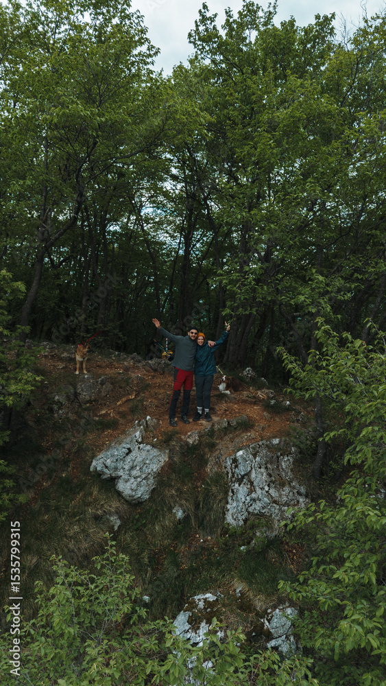 Fototapeta premium Couple and two dogs on rocky forest viewpoint on Ovcar mountain in Serbia, spring. Aerial view from drone. Hiking in Serbia in spring time
