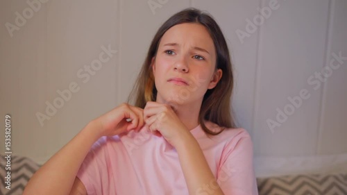 Young girl expresses dissatisfaction with her clothing by adjusting uncomfortable collar on white background