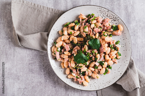 Close up of appetizing salad with tuna, white beans and greens on a plate on the table top view photo
