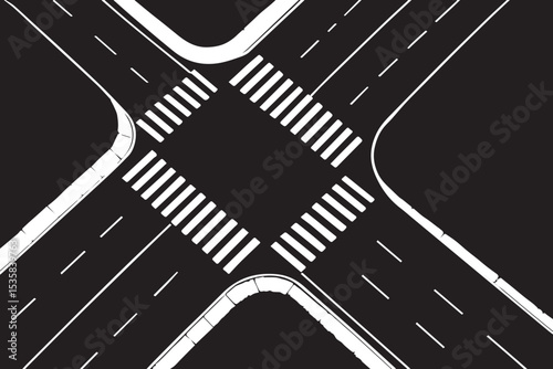 A top down aerial shot of a well maintained urban intersection, featuring white crosswalks, clear road markings, and green grass on the corners