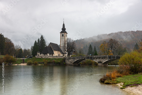 St. John the baptist's church rising from bohinj lake embankment on cloudy autumn day