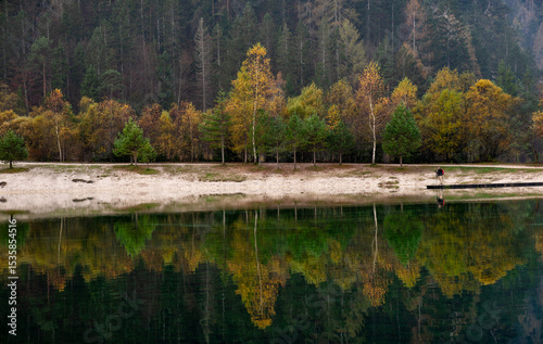 Autumn trees reflecting in the lake with photographer on pier
