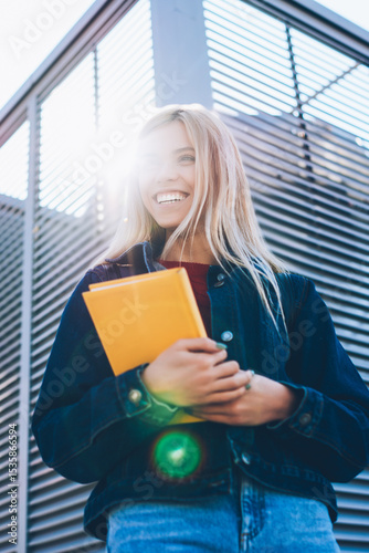 Good looking cheerful smart female student dressed in casual clothes sincerely laughing while strolling at sunny street.Attractive smiling blonde teenager having fun at urban setting during walk