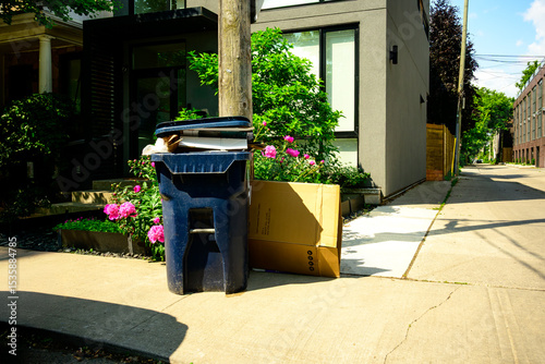 Recycling bin at the curb wsith flowers on a residential street waiting for municipal pick up on a bright summer morning shot in the Toronto Leslieville neighbourhood in June	

