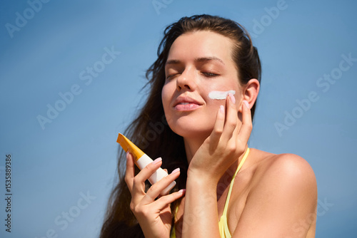 Billede på lærred Beautiful woman applying sunscreen on her face while enjoying a sunny day outdoors, promoting skincare and sun protection for healthy skin