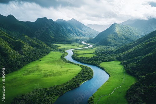 Aerial view of winding river flowing through lush green hills and mountains with fog lingering in the valleys in a tranquil landscape