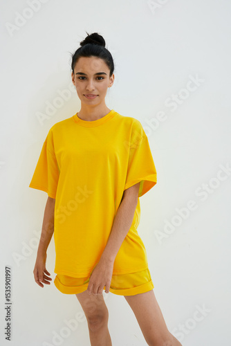 Young woman in bright yellow casual outfit poses confidently against white background, showcasing modern minimalism and vibrant summer fashion style.
