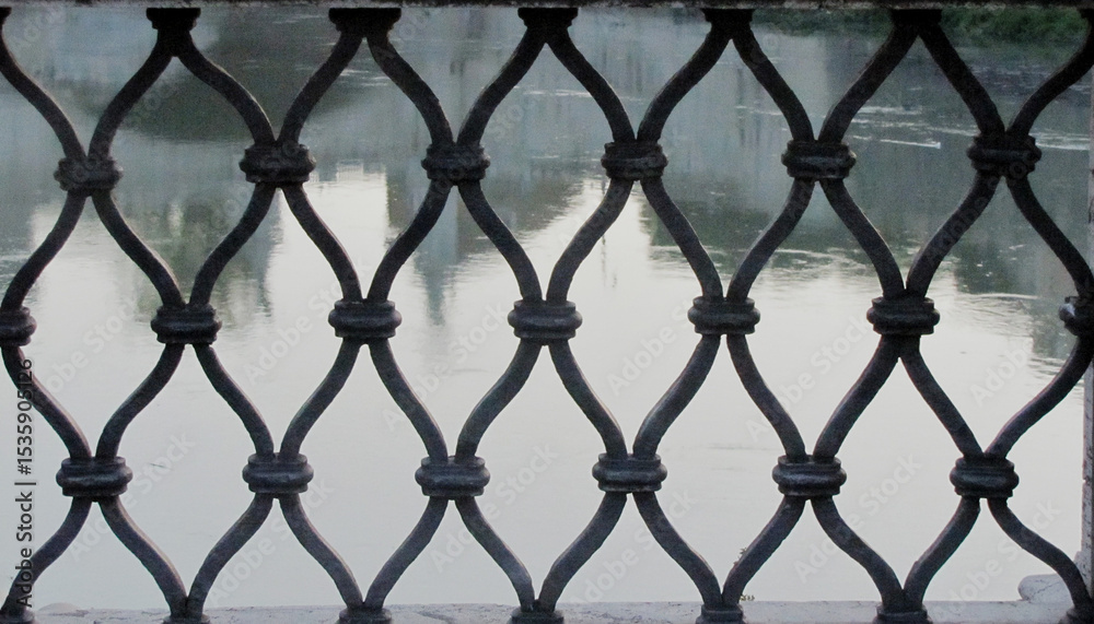 Fototapeta premium Geometric old-fashioned iron grate with the backdrop of calm river waters