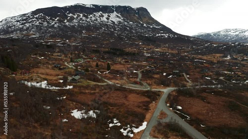 Mountainous landscape with scattered patches of snow and winding roads. Traditional Norwegian houses with grass roofs integrated into severe nature