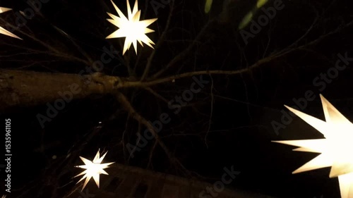 Christmas deco lanterns in the shape of a star on tree branches in the night sky.Festive Christmas street decorations. 4k footage